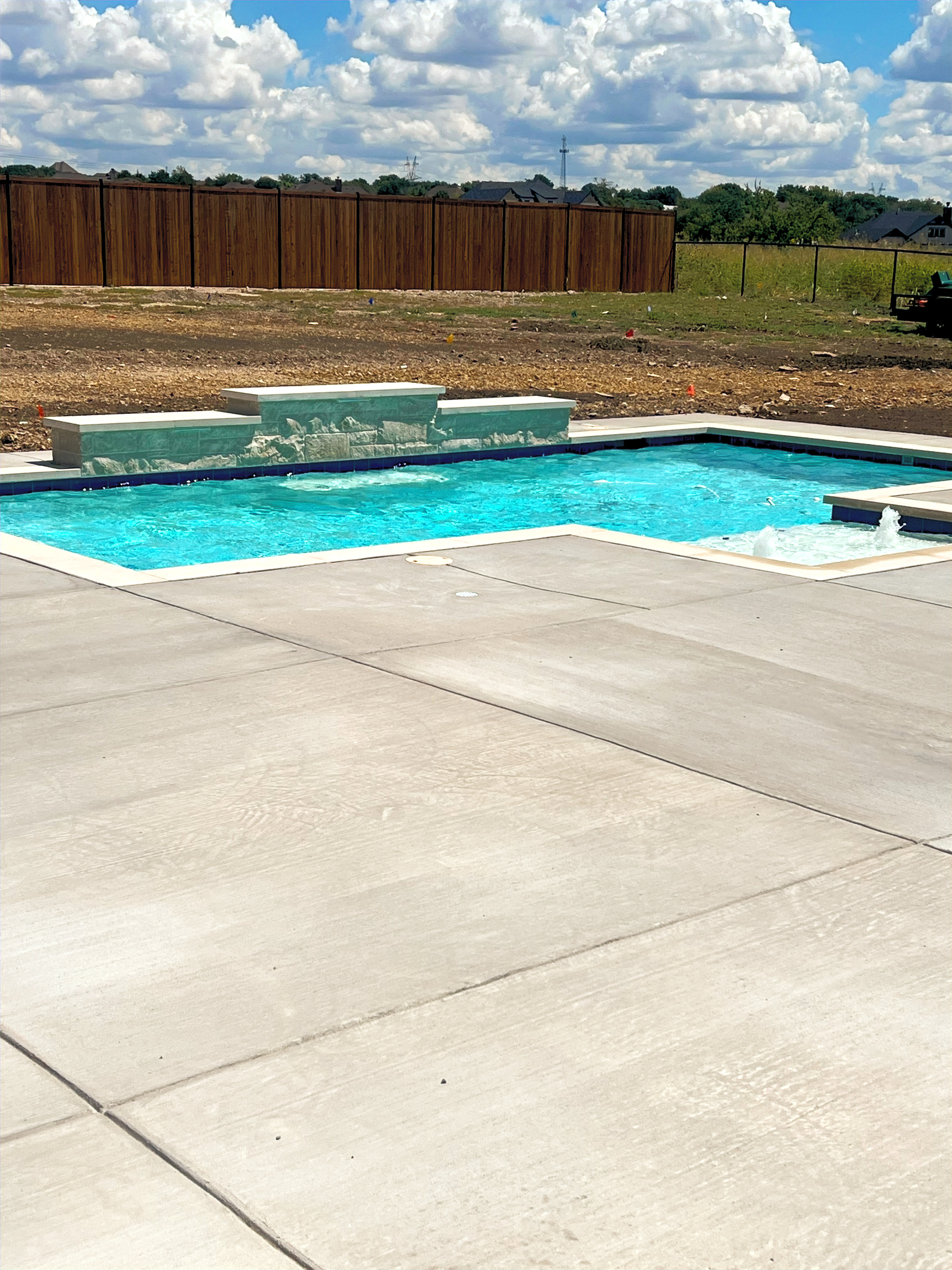 Rectangular turquoise pool with stone water wall and bubblers